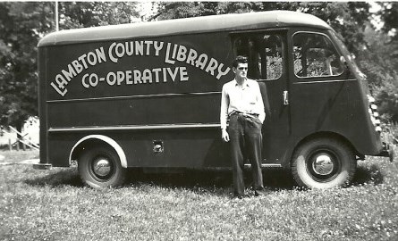 Black and white photo of a man standing in front of a van.